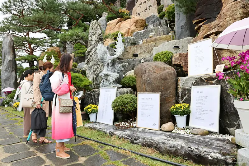 바위와 꽃 사이에 놓인 시 액자를 읽고 있는 관람객들